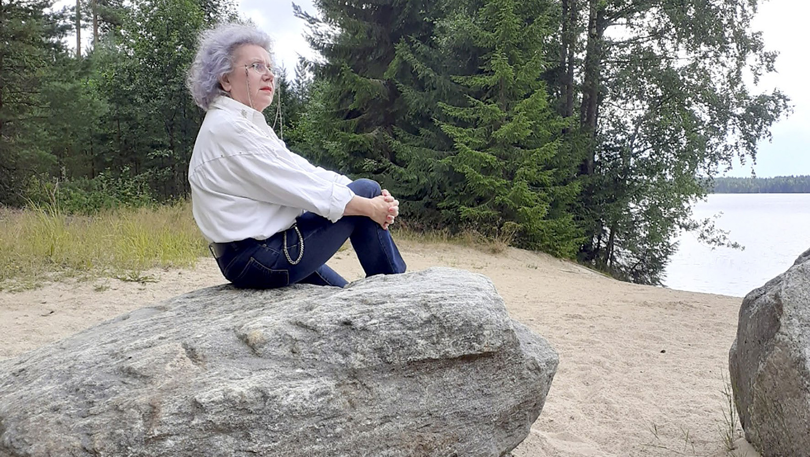Nainen rannalla kiven päällä istumassa