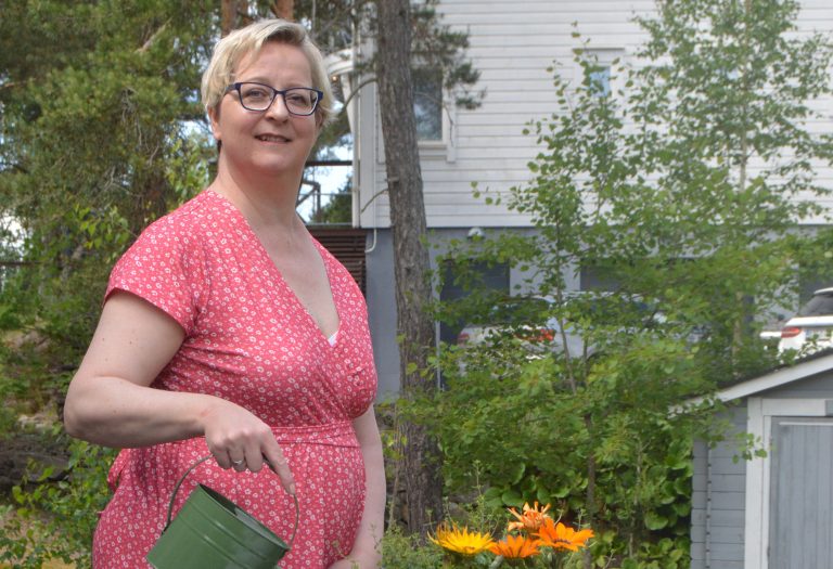 Nainen kastelee kesäkukkia pihallaan.