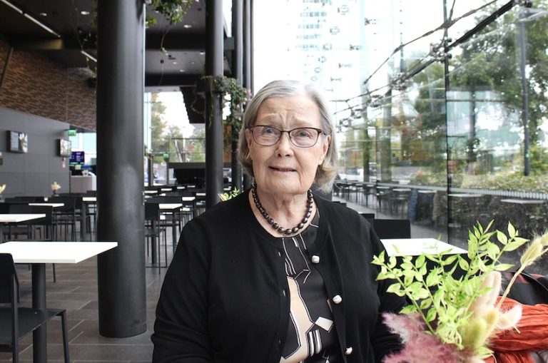 Vanhemppi nainen istuu Helsingin Musiikkitalon kahvilassa.