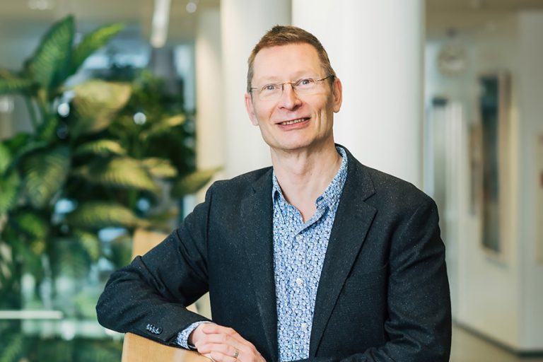 Silmälasipäinen mies seisoo suuressa aulatilassa.