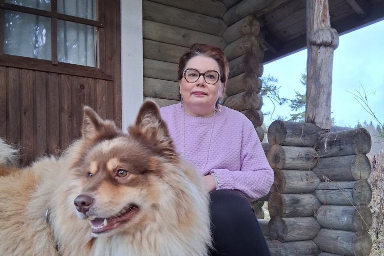 Nainen ja koira hirsimökin portailla.