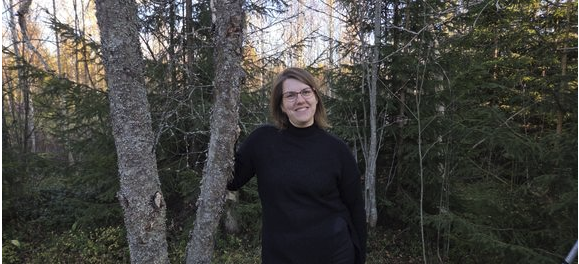 Tumma hymyilevä nainen seisoo syksyisessä säässä puun alla.